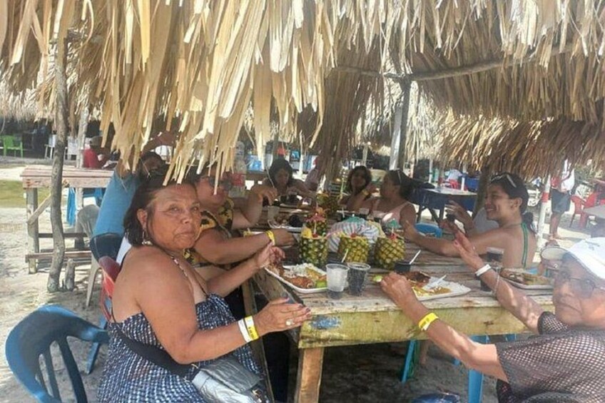 Mensen dineren onder een rieten dak, tafels zijn gedekt met borden eten en drinken. 2