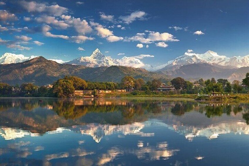A mountain range with snow-capped peaks, a calm lake reflecting the scenery, and a small settlement with buildings near the water's edge. 5