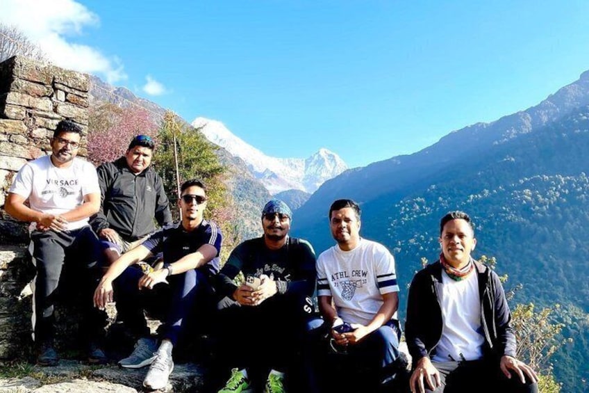 A group of people sitting on a stone ledge with a mountainous landscape in the background. 4