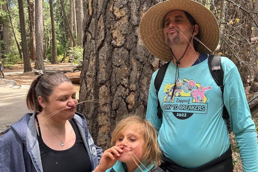 Three people standing in a forested area with trees and a road in the background. 2