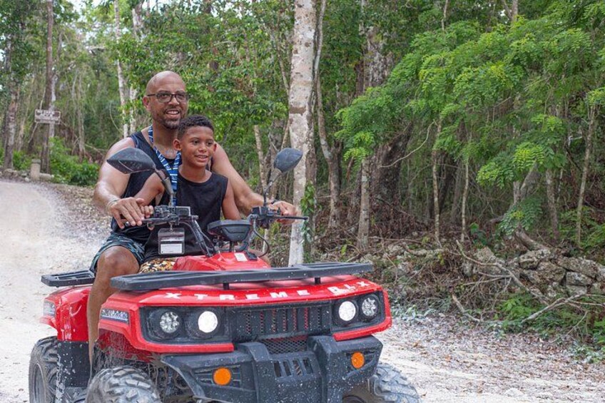 A person riding a red ATV on a dirt path surrounded by dense forest. 2