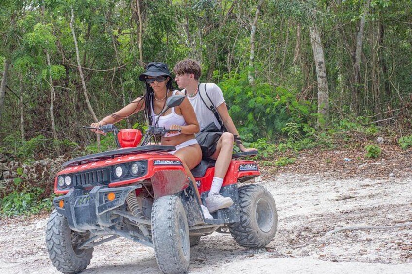 Two people on a red ATV on a dirt path surrounded by trees. 4