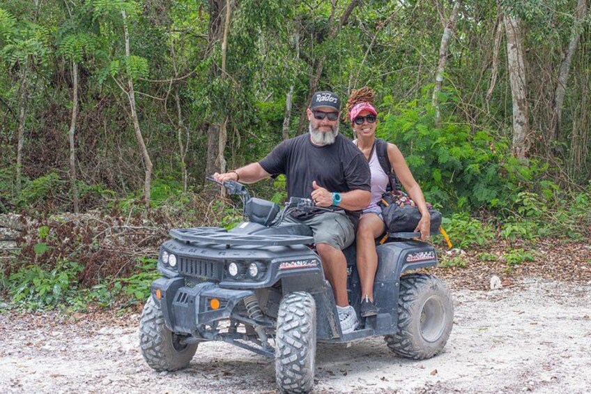 A man and a woman on an all-terrain vehicle in a forested area. 3