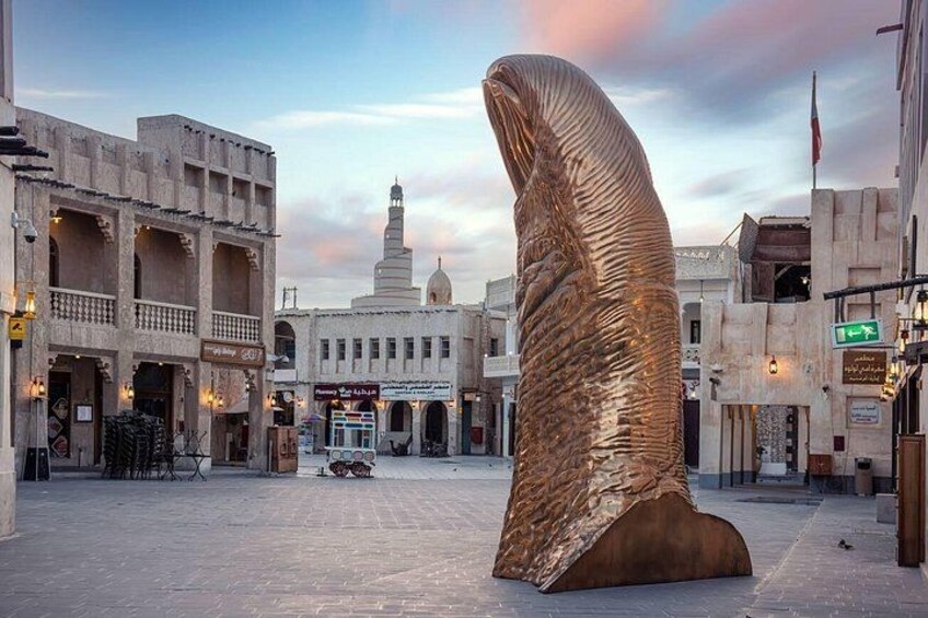 Een groot metalen beeld in een stadsplein met traditionele gebouwen en een minaret op de achtergrond. 5