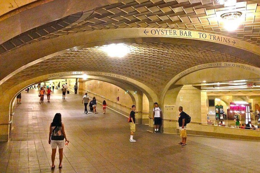 Una stazione della metropolitana con persone che camminano, un cartello di Oyster Bar e un cartello del servizio navetta Subway. 3