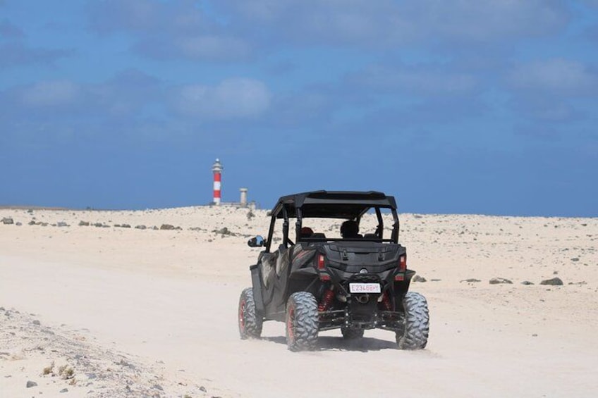 En sandbuggy kör på en sandstrand med en fyr i bakgrunden. 2