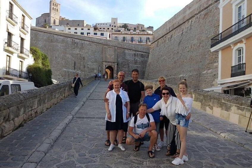 Un groupe de personnes posant devant un ancien mur de pierre, avec une vue sur la ville en arrière-plan. 1