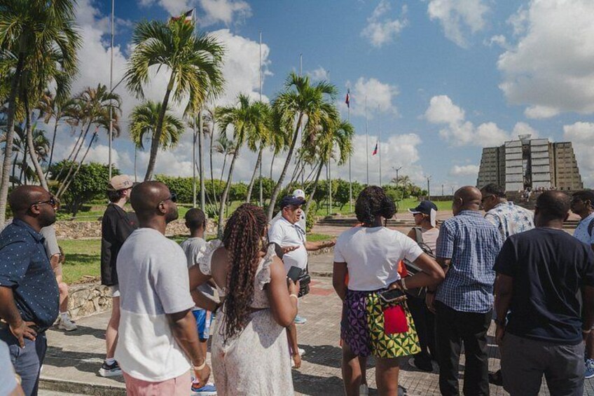 A group of people gathered outdoors, palm trees, and a large structure in the background. 4