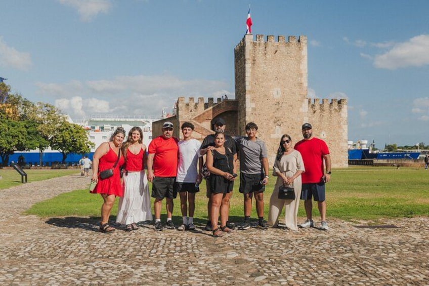 A group of people standing in front of a historic stone tower with a flag on top. 2
