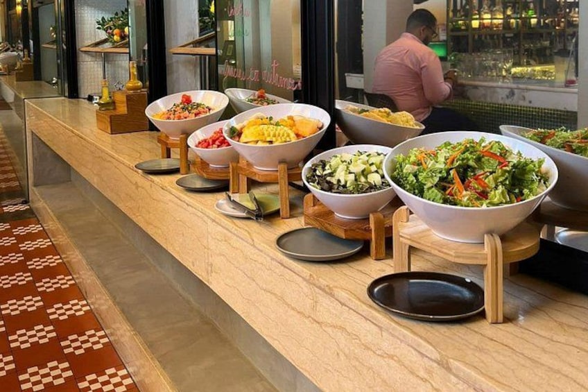 Een buffet met diverse gerechten in grote schalen, een betegelde vloer en een persoon op de achtergrond. 5