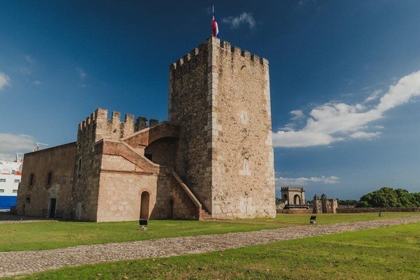 A historic stone castle with a tall tower, a flag, and a paved pathway. 3