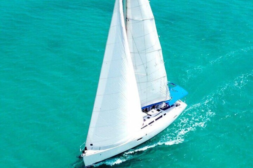 A sailboat with a white hull and blue sails on turquoise water. 1