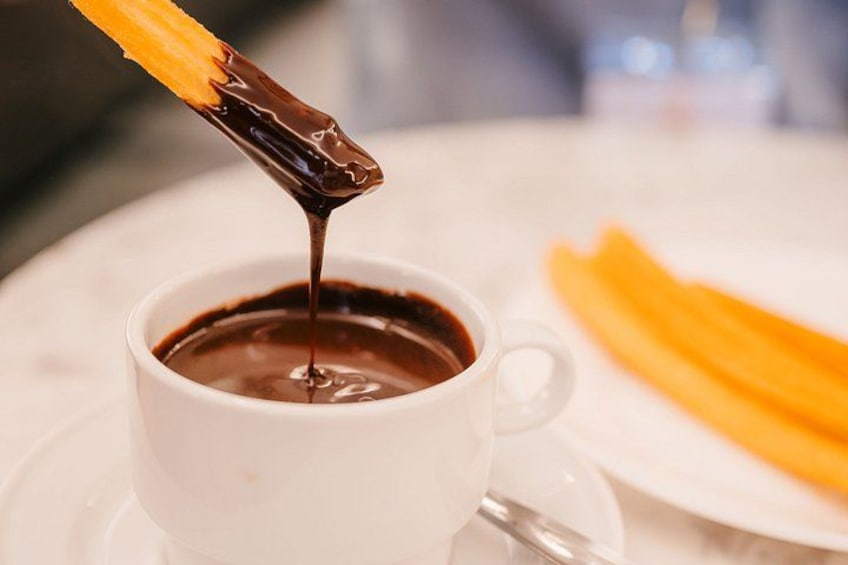 En kop varm kakao med en churro dyppet deri. 3