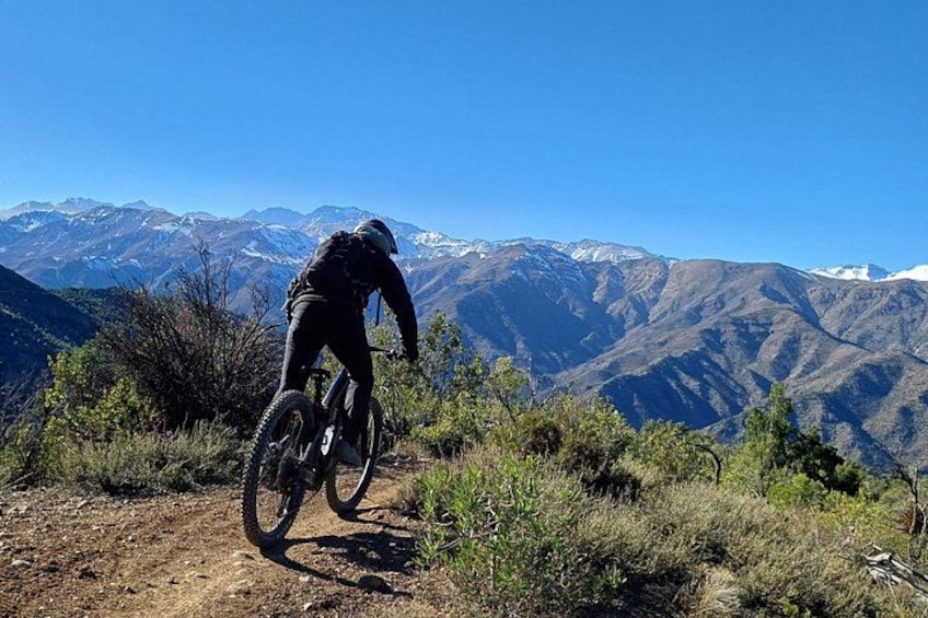 Eine Person fährt Mountainbike auf einem unbefestigten Weg, im Hintergrund eine gebirgige Landschaft. 1