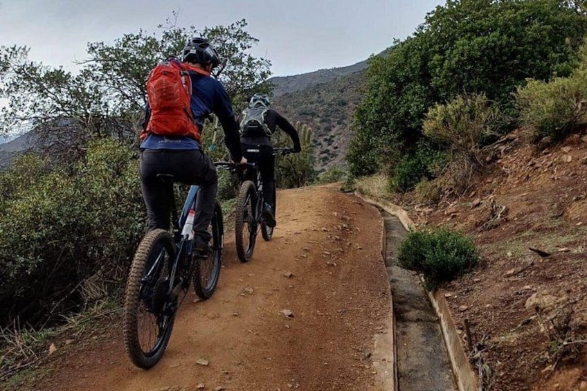 Twee fietsers op een zandpad, omringd door begroeiing en heuvels. 2