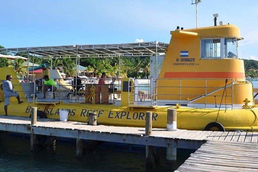 A yellow boat named 'Bays Islands Reef Explorer' docked at a pier with people around it. 1