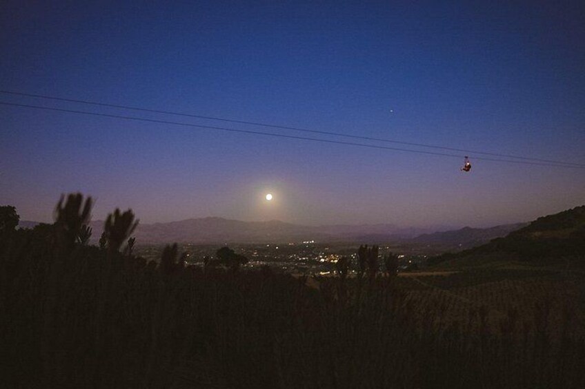 A night sky with a full moon, a distant cityscape, and a cable car in the sky. 5