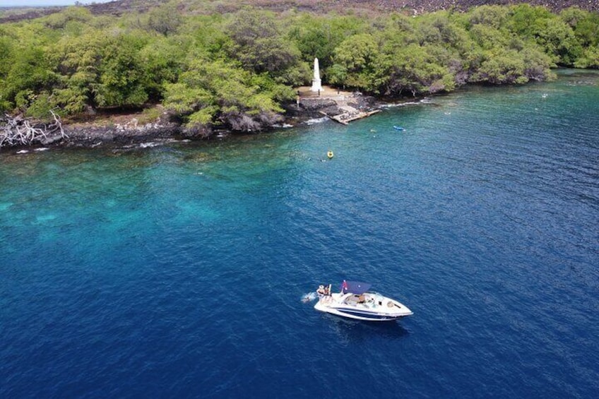 A boat on a clear blue sea with a lighthouse on a rocky shore. 1