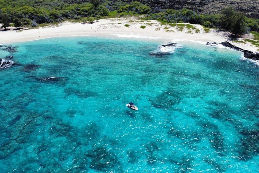 Une mer turquoise, un bateau, une plage de sable et des affleurements rocheux. 2