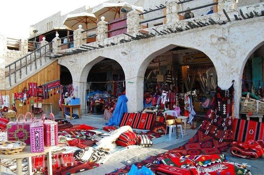 A market with colorful textiles and rugs displayed outside a building with arches. 3
