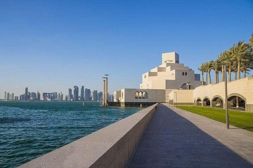 A waterfront promenade with a modern building, palm trees, and a city skyline in the background. 5