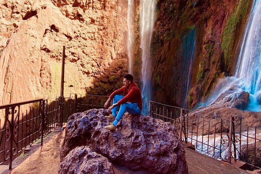 Une personne assise sur un rocher, près d’une cascade. 2