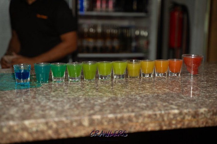A series of shot glasses with colorful liquids on a countertop. 2