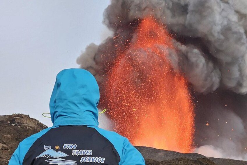 A person in a blue jacket observing a volcanic eruption with lava and smoke. 1