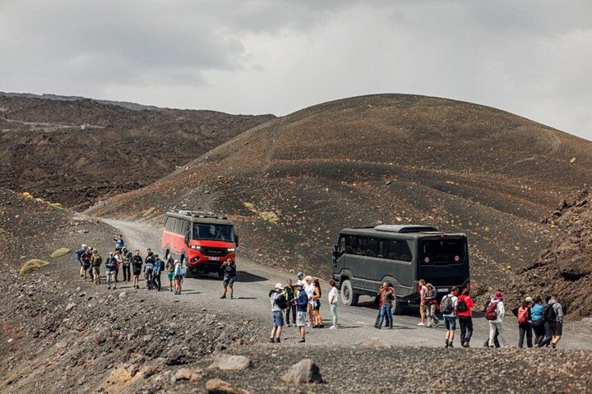A group of people standing on a rocky path with two buses parked on the side. 3