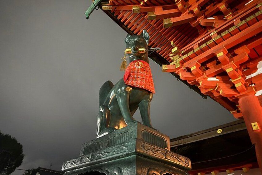 Een standbeeld van een persoon te paard, gekleed in een rode gewaad, met een traditionele dakconstructie op de achtergrond. 2