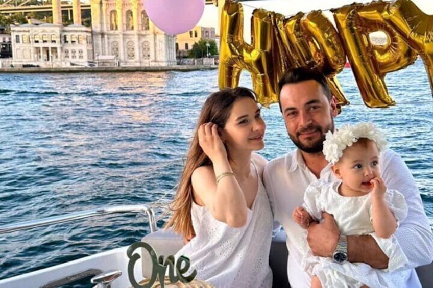 Una barca con una persona che tiene un bambino, un edificio sullo sfondo e palloncini con la scritta “HAPPY BIRTHDAY”. 3