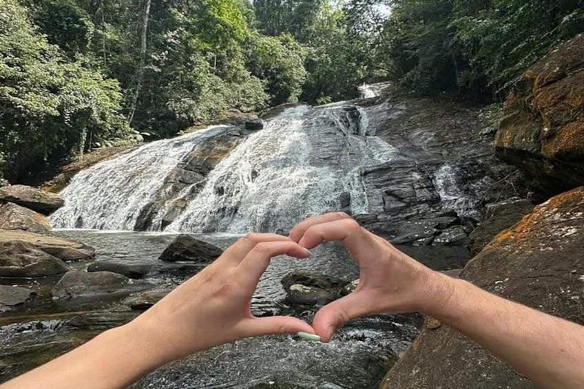 Hände formen ein Herz vor einem Wasserfall. 1
