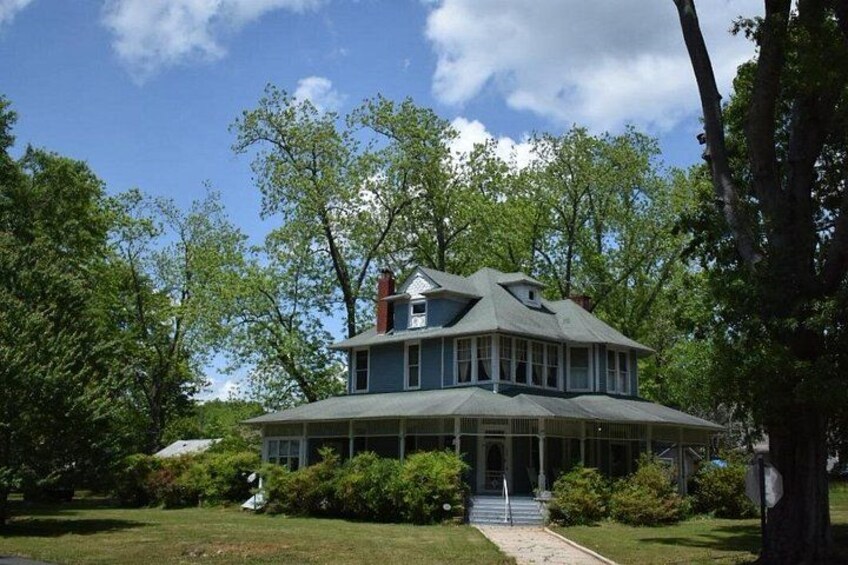 A large, two-story house with a wrap-around porch, surrounded by lush green trees and a well-maintained lawn. 2