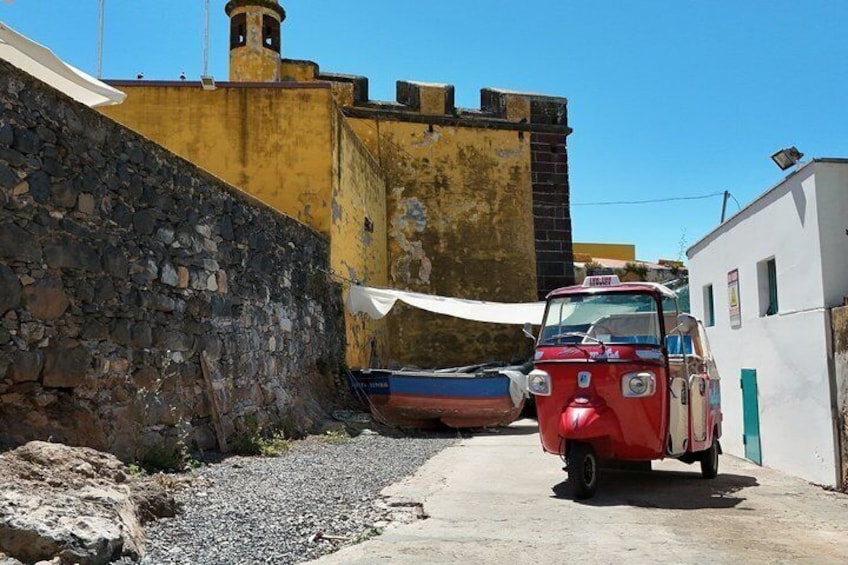 Un coche clásico rojo aparcado en un callejón estrecho, una pared de piedra y un edificio amarillo con una chimenea. 3