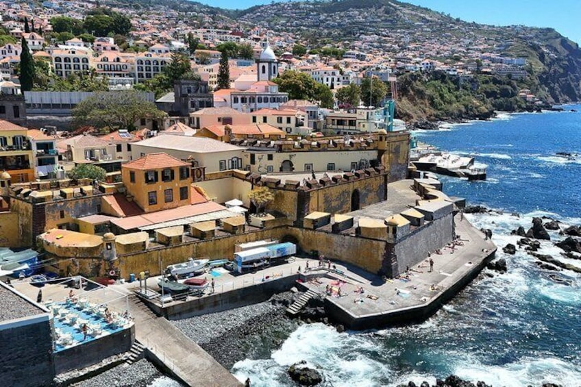 Un pueblo costero con una estructura fortificada, un puerto con barcos y edificios residenciales al fondo. 4
