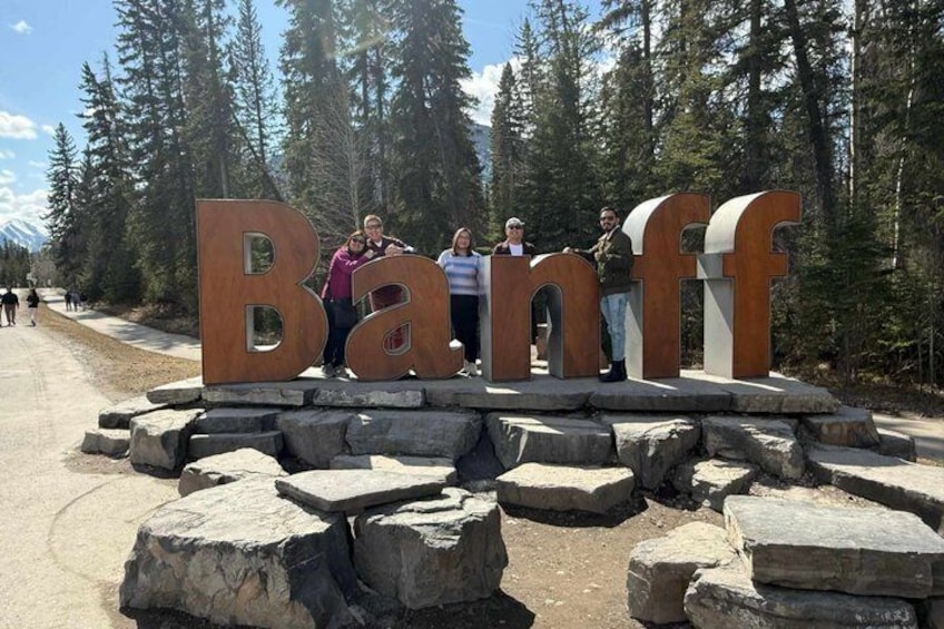 Un grupo de personas de pie frente a letras de madera grandes que deletrean 'Banff'. 3