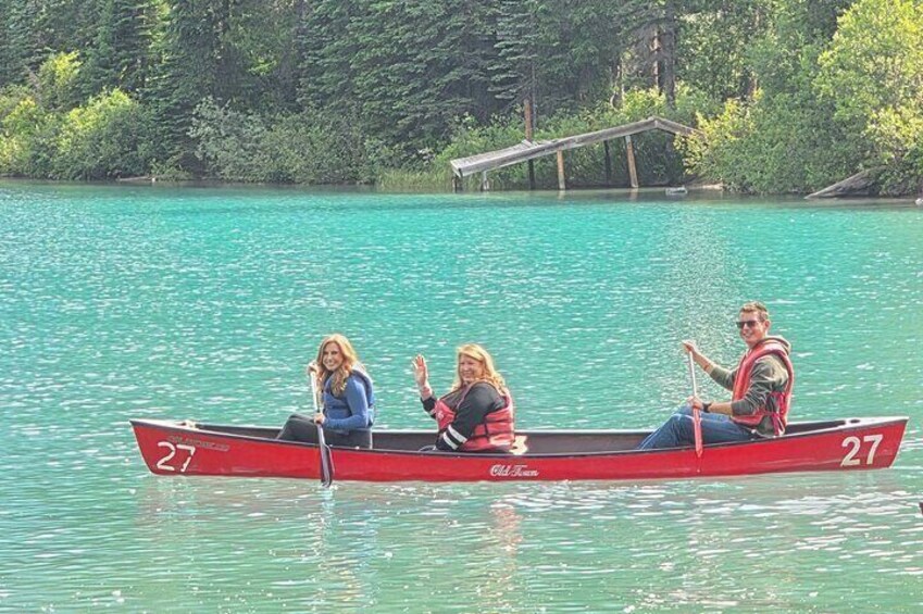 Tres personas en una canoa roja sobre un lago turquesa, con un puente al fondo. 2