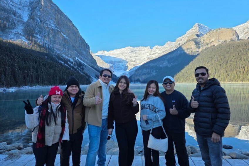 Un grupo de personas de pie en un muelle junto a un lago, con montañas al fondo. 4