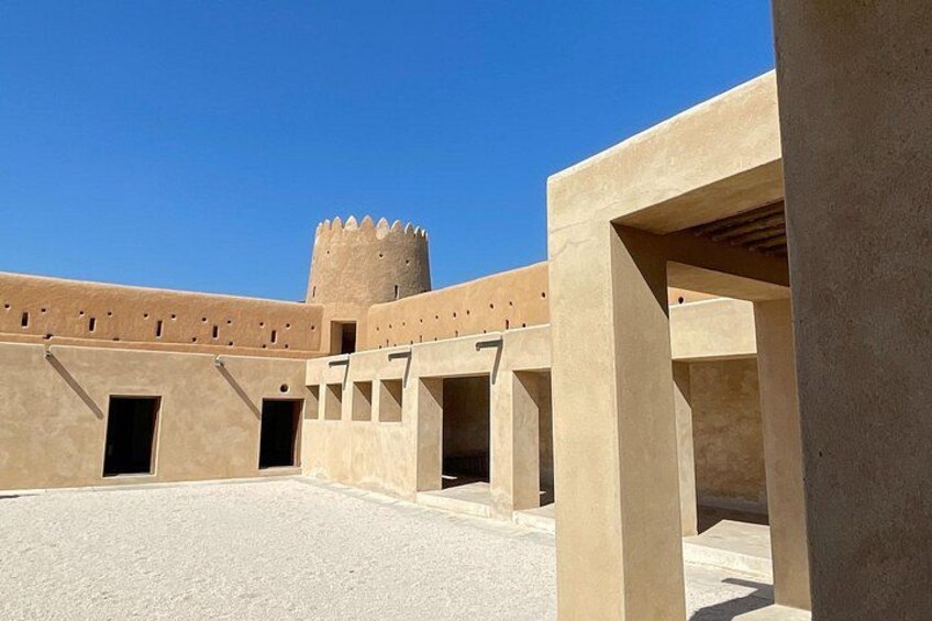 A courtyard with a tower, beige walls, and open spaces. 4