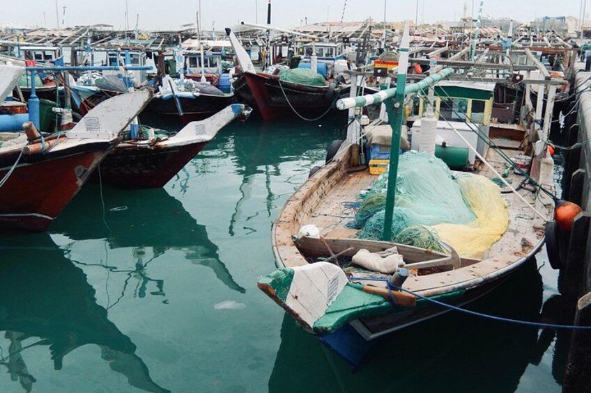 A harbor with multiple boats docked, fishing nets, and a green net on a boat. 1