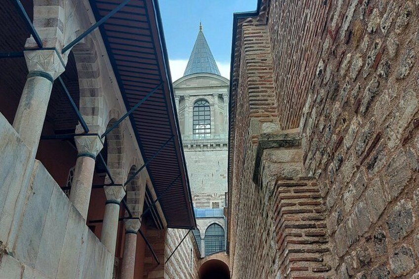 Une ruelle étroite bordée d’immeubles en pierre, une structure en forme de dôme visible au loin et un ciel bleu dégagé. 2