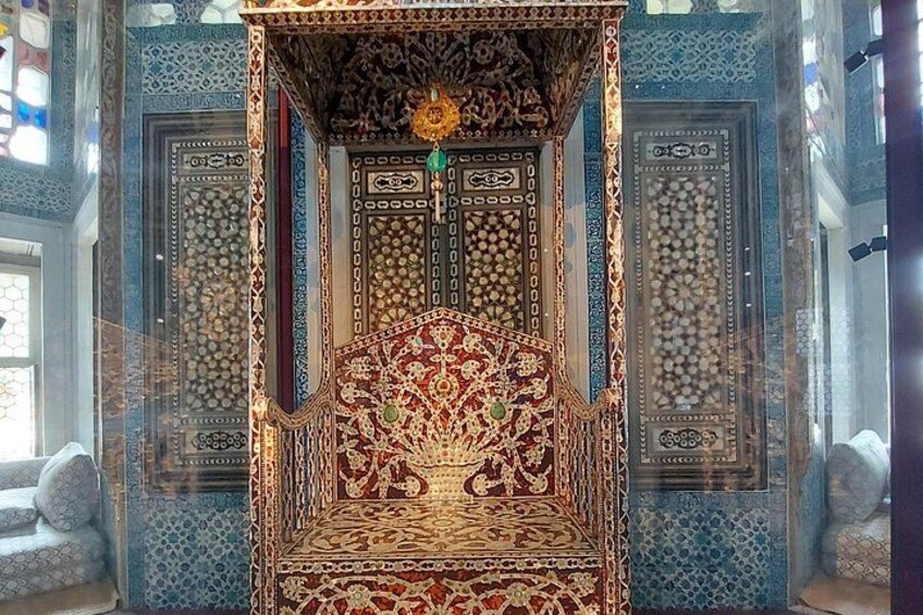 Une chaise en bois richement décorée, aux motifs complexes, avec un motif rouge et or, placée devant un mur aux motifs bleus et blancs. 3