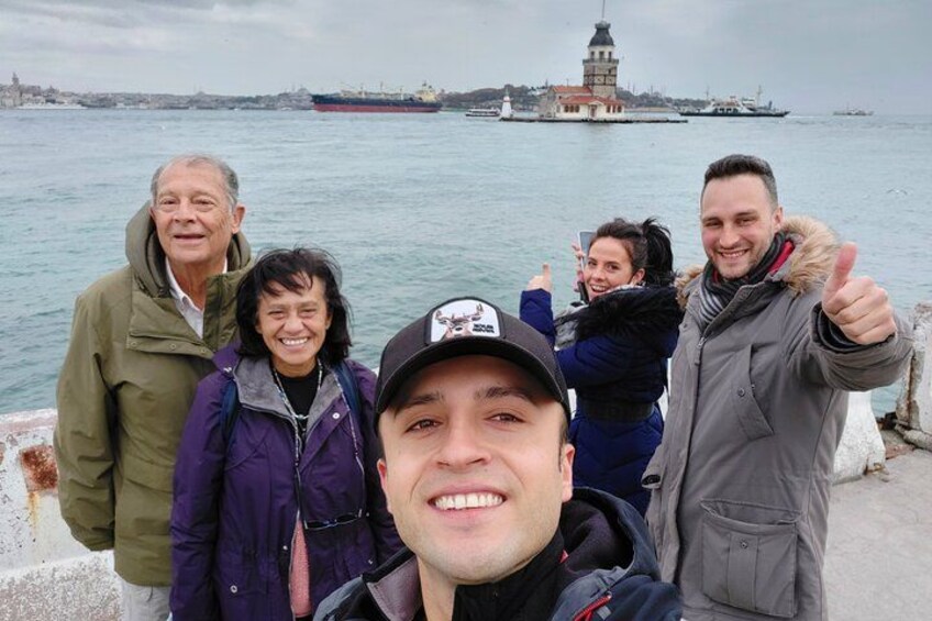 A group of people standing by a waterfront with a lighthouse and a ship in the background. 5