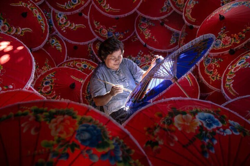 A person weaving a traditional blue and white fan among red floral umbrellas. 5