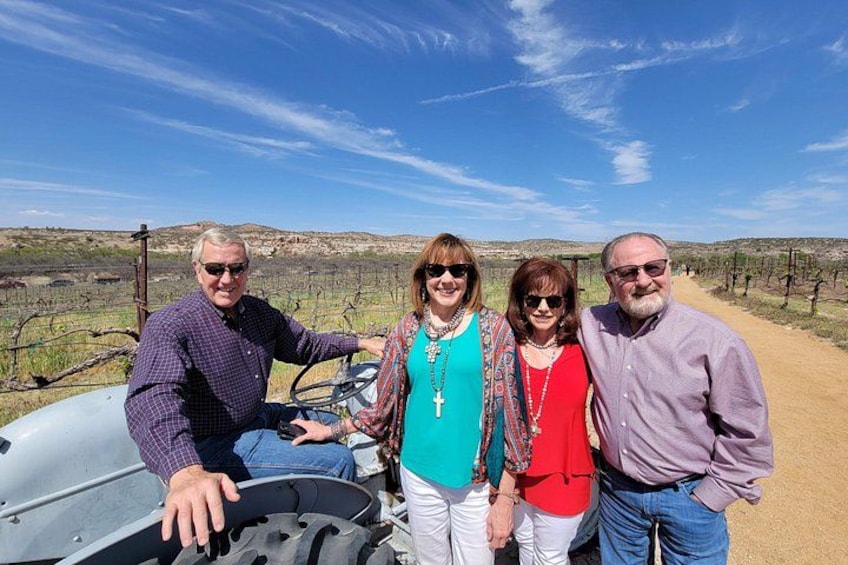 Four people standing in a vineyard with a tractor in the background. 2
