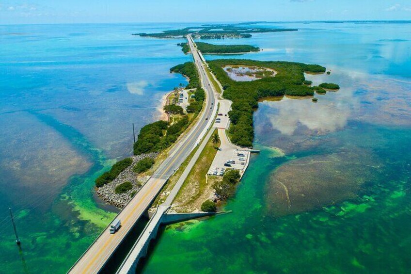 An aerial view of a coastal road with a bridge, surrounded by clear blue waters and green islands. 1