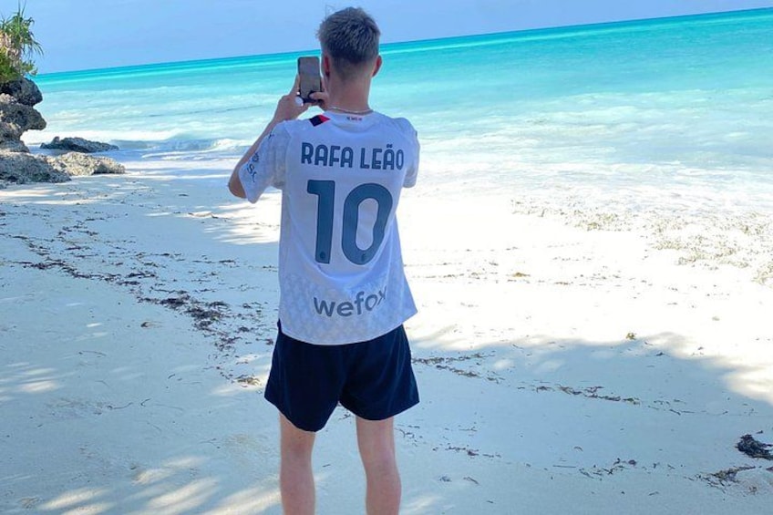A person taking a photo on a beach with clear turquoise water. 5