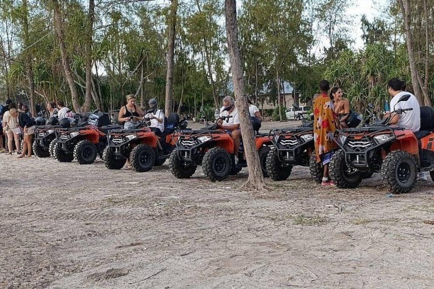 A group of people on ATVs lined up on a sandy beach with trees in the background. 2