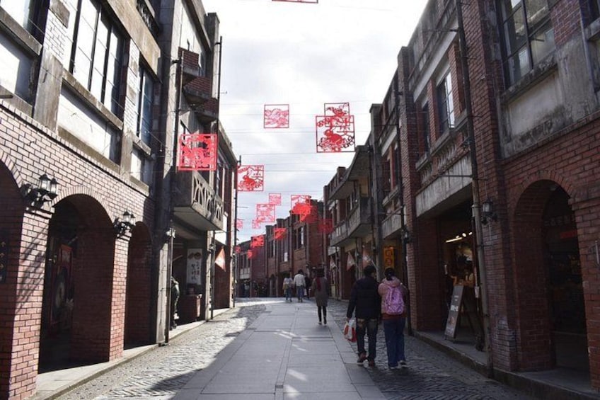 A cobblestone street lined with brick buildings, some with arched doorways, and red banners hanging from the buildings. 3