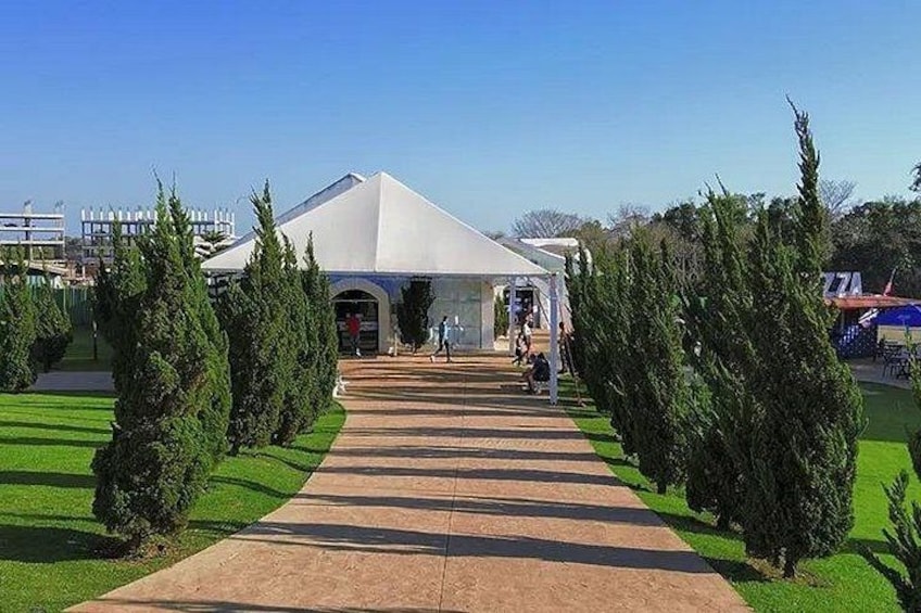 A pathway leading to a white tent-like structure with a peaked roof, surrounded by neatly trimmed evergreen trees. 5